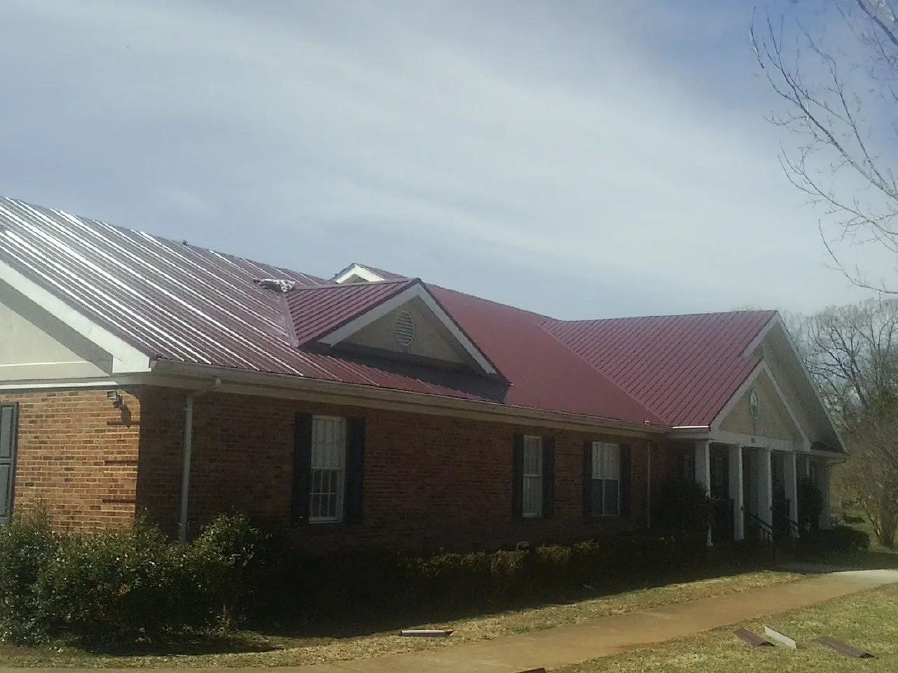 Red metal roof with gabled entries on a long brick building, from a Hail Damage Roof Repair job in White Earth