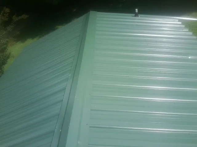 New green metal panels meeting at the ridge of a roof — Flat Roof Repair work by our crew in White Earth