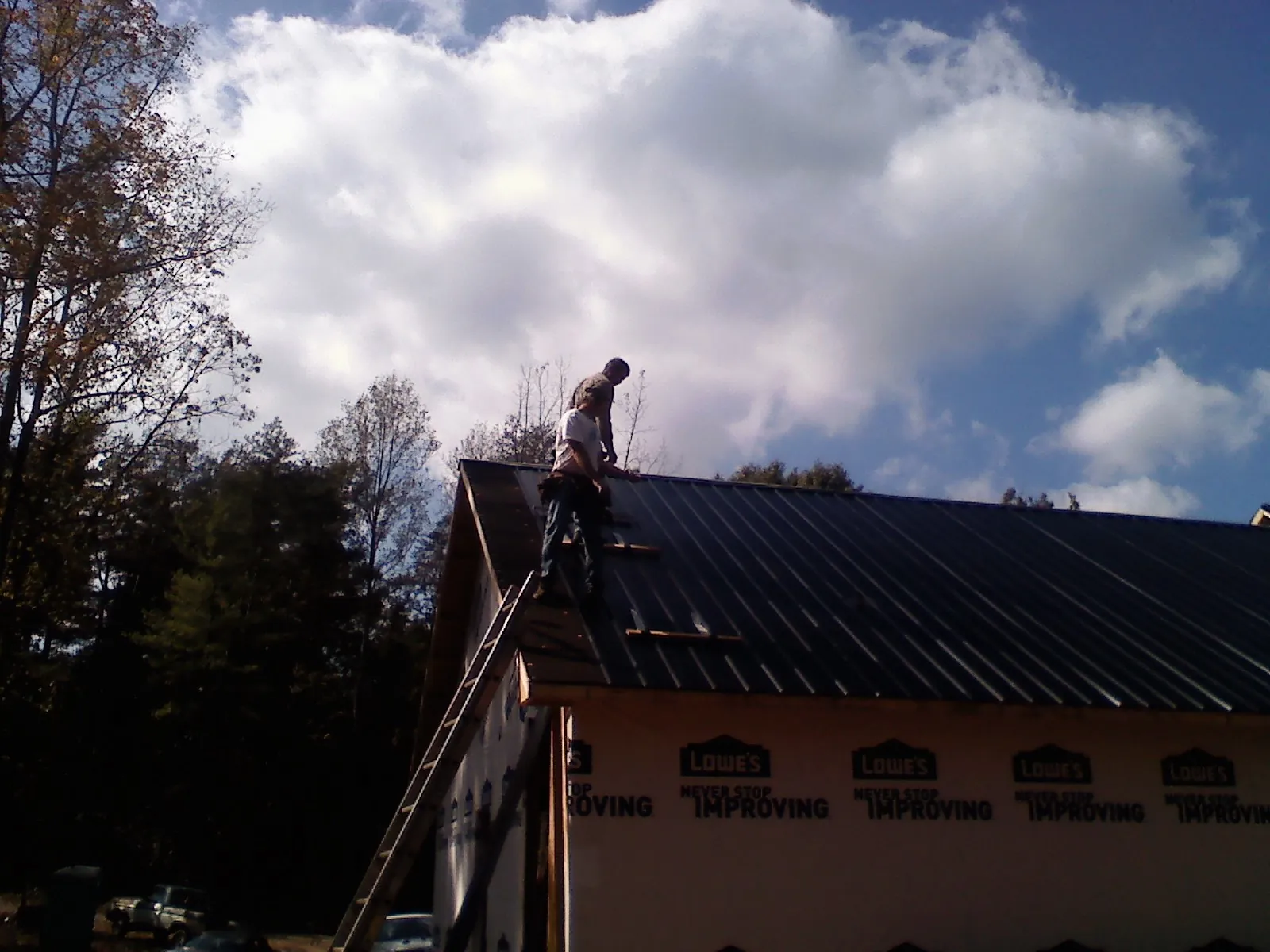 Roofer fastening dark metal panels high against a cloudy sky, from a Roof Inspection job in White Earth