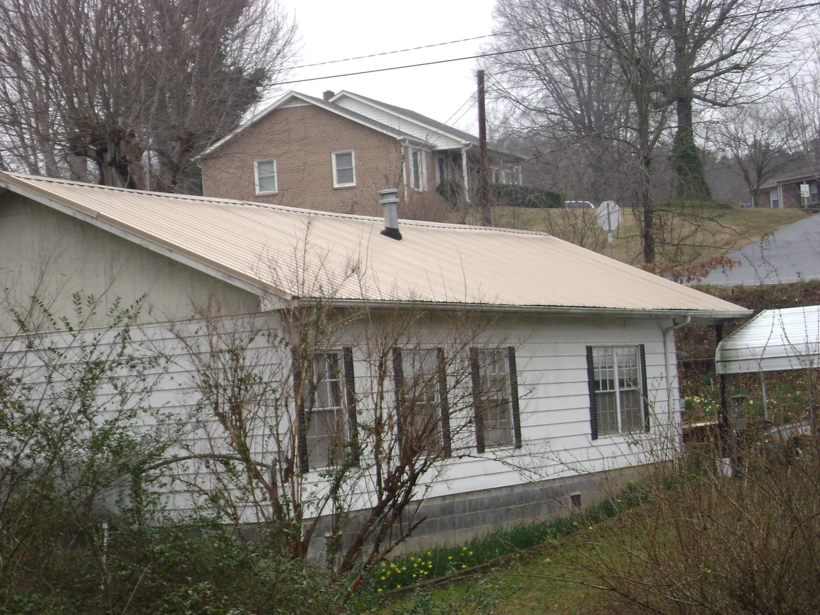 Tan metal roof on a white sided house set into a hillside — Commercial Roofing by Roofing Brothers in White Earth